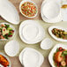 A table with Acopa Nova cream white bowls and plates on it.