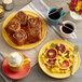 A plate of food and coffee on a table with a yellow Acopa Capri stoneware plate.