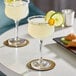 Two Acopa Deco cocktail glasses filled with yellow drinks on a table