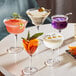 A table with Acopa Deco cocktail glasses filled with different colored drinks and garnishes.