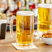 An Acopa beer mug filled with beer on a table with a bowl of pretzels.