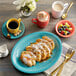 An Acopa Capri Caribbean turquoise oval stoneware platter with a plate of food and a cup of coffee on a table.