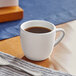 An Acopa bright white stoneware espresso cup on a table with a cup of coffee.