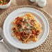 An Acopa Capri stoneware plate with spaghetti and meat sauce and cheese on a table.