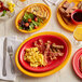 An oval table set with Acopa Capri Passion Fruit Red Stoneware plates filled with food and drinks.