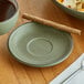 A Moss Green Acopa Embers stoneware saucer with a cup of coffee on a table.