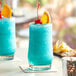 Two Acopa Saloon beverage glasses filled with blue drinks, orange slices, and cherries on a table in a cocktail bar.