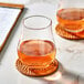 A close-up of an Acopa Select Stemless Belgian Beer/Tulip Glass filled with brown liquid on a table with a coaster.