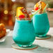 Two Acopa stemless tulip glasses filled with blue drinks and fruit on a table in a cocktail bar.