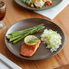 An Acopa Embers hickory brown stoneware coupe plate with rice, asparagus, and salmon on a table.