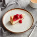 A slice of cheesecake with cherry sauce on an Acopa Keystone Vanilla Bean coupe plate.