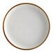 An Acopa Keystone stoneware coupe plate in vanilla bean with brown specks on the rim.