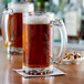 Two Acopa beer mugs on a table filled with beer.