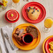 An Acopa Capri passion fruit red stoneware monkey dish on a table with a plate of scrambled eggs and a red cup of coffee.