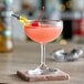 A pink cocktail in an Acopa coupe glass with a cherry and a straw.