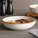 Two Acopa Keystone Vanilla Bean Stoneware coupe low bowls filled with food on a table.