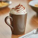 A close-up of a cup of hot chocolate with whipped cream in an Acopa Embers hickory brown matte stoneware mug.