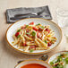 A close up of an Acopa Keystone Vanilla Bean stoneware coupe plate with pasta and salad on it.