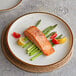 A close-up of a Acopa Keystone Vanilla Bean Stoneware Coupe Plate with salmon and asparagus on it.