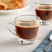A close-up of two Acopa espresso cups on a table with a glass of coffee.