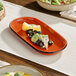 An orange stoneware oblong coupe platter with a sample serving of cheese, fruit, and herbs.