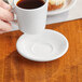 A person holding an Acopa bright white stoneware saucer with a cup of coffee.