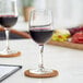 Two Acopa Select Flora wine glasses on a wooden coaster on a table with a glass of red wine.