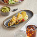 An Acopa Granite Gray Stoneware oblong coupe platter on a table with tacos, guacamole, and a drink.