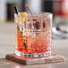 An Acopa Madras rocks glass filled with a red drink and straws on a stone coaster.