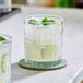 A clear Acopa Madras 11 oz. rocks glass filled with a light-colored beverage, ice, and garnished with mint, placed on a coaster.