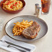 An Acopa Keystone granite gray stoneware coupe plate with steak and french fries on it on a table.