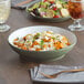 A bowl of pasta in an Acopa moss green stoneware bowl on a table with salad and a glass of wine.