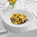 A white Acopa Liana porcelain pasta bowl filled with pasta, mushrooms, and herbs on a table.