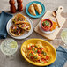 An Acopa Citrus Yellow oval stoneware platter with tacos, chips, and a bowl of soup on a table.