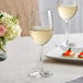 An Acopa Covella wine glass filled with white wine on a table.