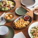 An Acopa Embers moss green matte coupe stoneware plate on a table with food and drinks.