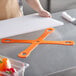 A person with a Mercer orange cutting board on a kitchen counter.