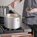 A person cooking food in a Choice aluminum sauce pan on a stove.