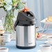 An Acopa stainless steel decaf airpot on a table with a cup of coffee.