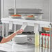 A woman wearing gloves holds a receipt over a Choice aluminum wall mounted ticket holder on a shelf above food.