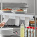 A woman's hand slides a paper into a Choice aluminum wall mounted ticket holder above a counter with food.