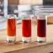 A group of glasses with different colored liquid, including a glass of amber liquid.