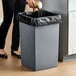 A gray square 25-gallon trash can with a black liner.
