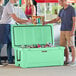 A group of men standing next to a CaterGator seafoam green cooler filled with cans and bottles.