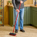 A person using a Libman red floor scrub to clean the floor.