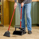 A person using a Libman lobby broom and dustpan to sweep a floor in a professional kitchen.