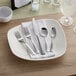 A plate with Acopa Ridge stainless steel flatware and a napkin on it.