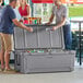 Two men standing next to a CaterGator outdoor cooler full of cans.