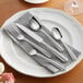 A white plate with Acopa Harmony stainless steel flatware on it.
