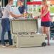 A man and woman standing next to a CaterGator outdoor cooler filled with bottles.